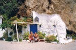 Couple in beach with tiny white house with blue door built into cliff in Spain