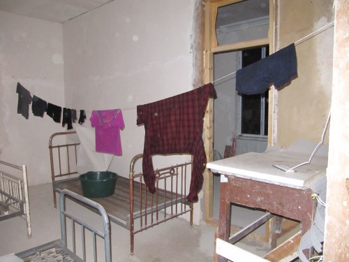Clothes hang-drying on a line in a dusty room with cots at night 
